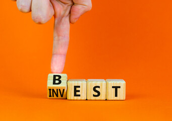 Best invest symbol. Businessman turns a wooden cube and changes the word Invest to Best. Beautiful orange table, orange background. Business and best invest concept. Copy space.