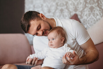 Indoor portrait of young father hugging his little baby daughter