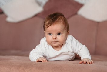 Baby girl wearing white clothes in sunny nursery room. Newborn child relaxing on sofa.