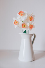 Beautiful bouquet of fresh white and orange daffodil flowers in full bloom in vase against white background. Copy space for text. Spring blossoms. Still life with bunch of narcissuses.