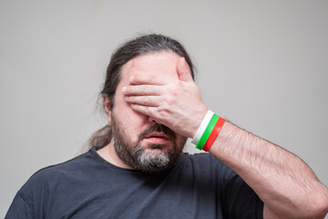 Fototapeta premium An unshaven man with bracelets in the colors of the Bulgarian flag pathetically closes his eyes with his palm.