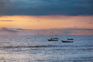 Evening view of the Pacific Coast in Tarcoles, sunset, glittering waves and fisherman boats. Idyllic sunset landscape. Tarcoles, Costa Rica. Pura Vida concept, travel to exotic tropical country.