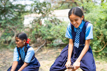 girl kids in uniform playing on seesaw game at school playground - concept of break time, leisure...