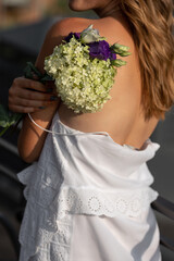 Beautiful blonde woman with curly hair in a white dress with a hydrangea close-up. Back view. Sunny summer day. No face. soft focus