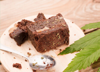 piece of brownie with marijuana, on wooden board with spoon and green cannabis leaf