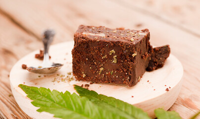 piece of brownie with marijuana, on wooden board with spoon and green cannabis leaf