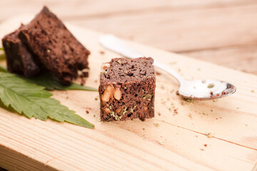 piece of brownie with marijuana, on wooden board with spoon and green cannabis leaf