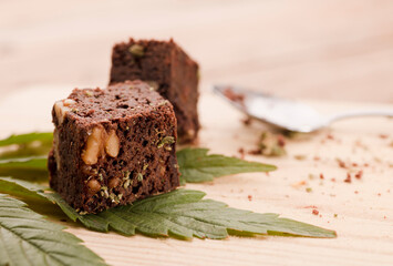 piece of brownie with marijuana, on wooden board with spoon and green cannabis leaf
