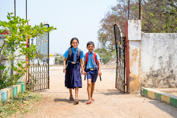 Happy teenager sibling kids in uniform entering to school from gate - concept of education, back to...