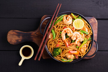 Stir-fried spaghetti or stir-fry noodles with vegetables and shrimp in a black bowl. dark background, top view