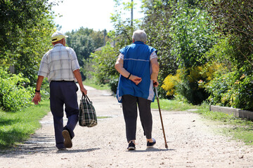 Elderly couple walking on a rural street. Old man and woman with cane together, life in retirement