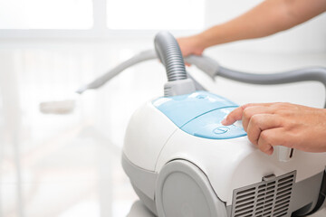 Close up hand a man push power switch of the vacuum cleaner to suck up fur cat to clean the house floor and blur home an interior in the background