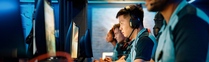 Selective focus on determined Asian cybersport player participating in online video games competition with blurred team members on background © Yaroslav Astakhov