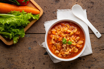beef and tomato macaroni soup in white bowl on wood table.Top view