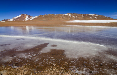 Desolate mountain landscape in the high Andes in the north of Chile with volcano and a small frozen lake