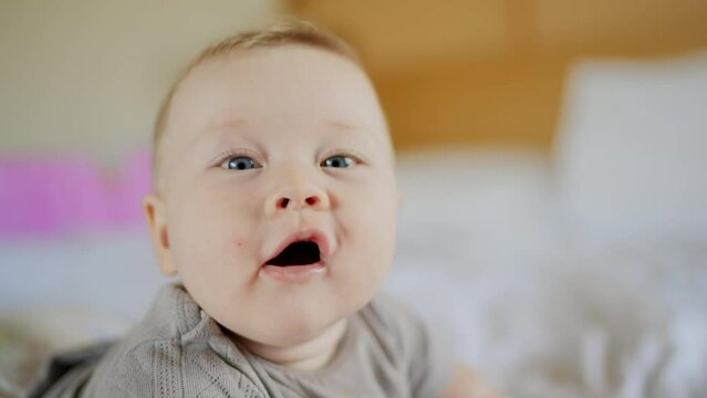 Funny little baby boy smiling looking at camera at home, cute kid talking to webcam with sound making online video call or recording vlog having fun, child with pretty face waving hand sitting on sofa