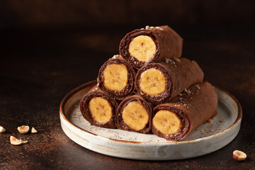 Banana stuffed chocolate crepes on a dark background. Vegan, plant based food. copy space