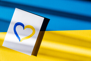 Top view of painted yellow and blue heart sign on card on ukrainian flag.