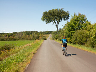 Obraz premium a single woman from the back, doing gravel bike on a quiet countryside road, on a summer sunny day