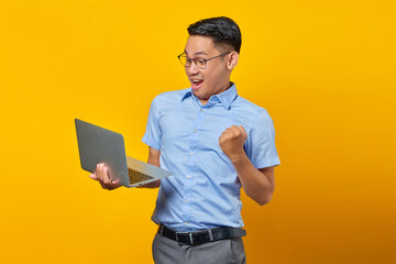 Excited young asian man Asian in glasses using laptop isolated on yellow background. businessman and entrepreneur concept