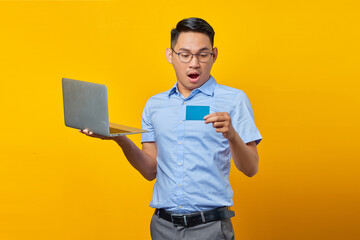 Surprised young asian man Asian in glasses holding laptop and looking  credit card isolated on...