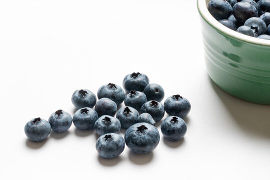 Fresh and juicy blueberries from a green clay bowl spread on a white background.