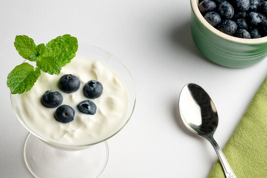 Blueberry and yoghurt desert with mint in a fine glass dish on a white background. A clay bowl with blueberry in it.