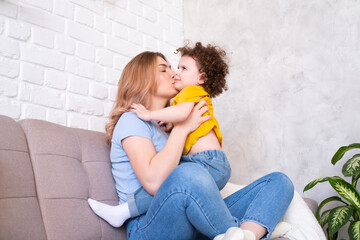 young women plays with her curly child daughter on couch, they laugh, hug and have fun together