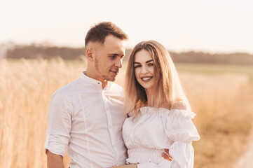 Handsome guy and blonde girl walking on the field of wheat on a beautiful warm sunset.