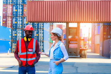 An African American male employee or supervisor and a Caucasian woman wear a safety vest and stand speaking