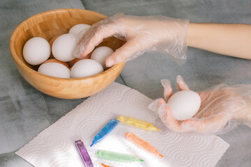 Child's hands paint Easter egg next to the next to a bowl with white and brown eggs...