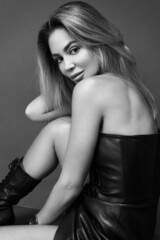 Sexy woman in leather clothes posing against grey studio wall. Black and white.