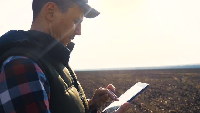 man farmer red neck with a digital tablet walking on lifestyle land for sewing on a soil black field. eco farming agriculture concept. male worker studies winter dirt soil wheat crops works in field