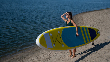 Caucasian woman walks along the beach and carries a sup board on the river in the city. Summer...