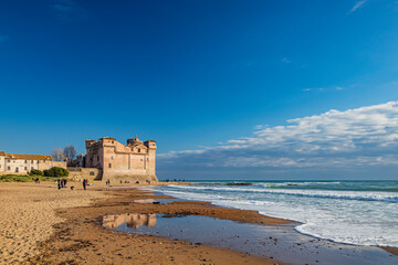 Santa Marinella, Rome, Lazio, Italy - The seaside castle of Santa Severa on a cold winter day. The rough sea, the strong wind, the cloudy blue sky. Many people stroll and enjoy the sun on the beach.