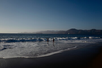Fototapeta na wymiar Ocean water as waves with human children swimming and sailboat in distance.