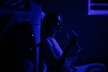 Obraz na płótnie Canvas Sad woman drinking wine while sitting near the refrigerator in the dark.