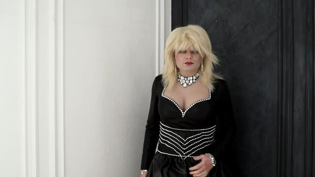 Confident transvestite walks in front of the camera. Full length transvestite in a beautiful dress. Portrait of a transvestite in full growth. A man dressed as a woman, wearing a white wig.