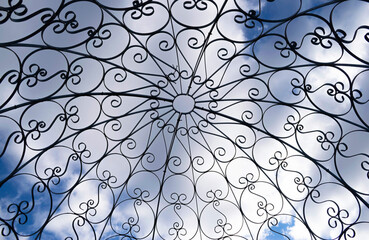 Abstract garden gazebo dome close up against a blue sky with clouds. 
