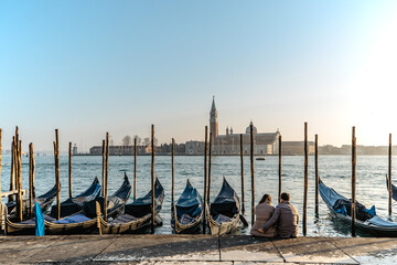 Couple in love having date in Venice,Italy.Famous canal and traditional gondolas,San Giorgio Maggiore church in background.Venetian city lifestyle,travel scenery.Architecture and landmark of Venezia.