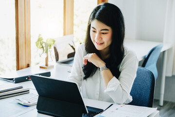 A female entrepreneur or businesswoman shows a smiling face while using a tablet computer for video conferance working on a wooden table.