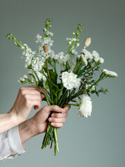Hands arranging a bouquet of white flowers against green background