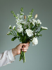 Hand offering a bouquet of white flowers against a wall