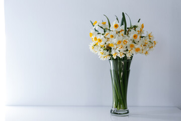 A bouquet of white daffodils in glass vase on the table, natural sunlight. Narcissus flowers in...