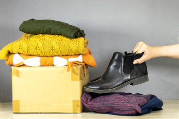 carton box with used clothes for donation,  woman holding ankle boots.  collection and support of...