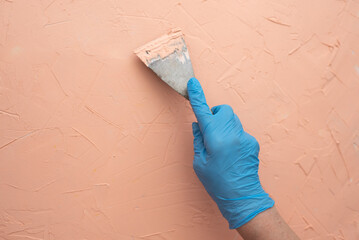 Woman's hand in blue glove with putty knife make by putty interesting diverse peach texture on...