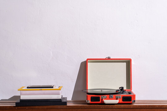 Pile of books and a retro turntable on a wooden shelf against a white wall. Record player. High quality photo