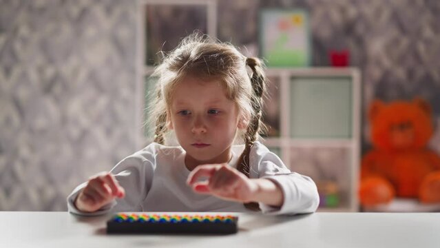 Upset little girl student plays with toy abacus learning mental arithmetics at table in kindergarten classroom close view slow motion