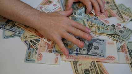 Close-up of male hands raking and pulling a bunch of money from Russian five thousandth bills and American dollars. Greed, bribery and corruption - obrazy, fototapety, plakaty