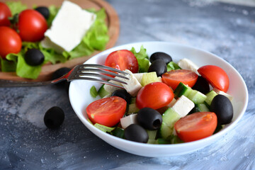 greek salad with cherry tomatoes, feta cheese, cucumber and olives in bowl with fork, close-up 